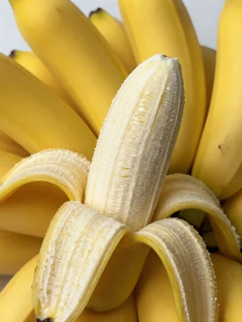 Verse banaan heel en in plakjes, in een kom en op een rustieke tafel