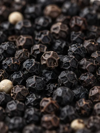 Zwarte peperkorrels en gemalen peper in een keramisch kommetje en op een houten oppervlak